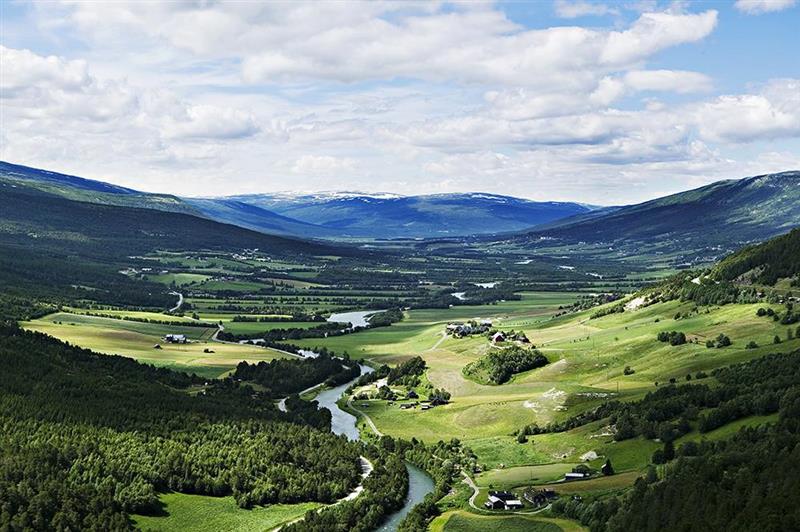 Utsikt over grønne marker i dalføret Lesja, med blå fjell og himmel i horisonten